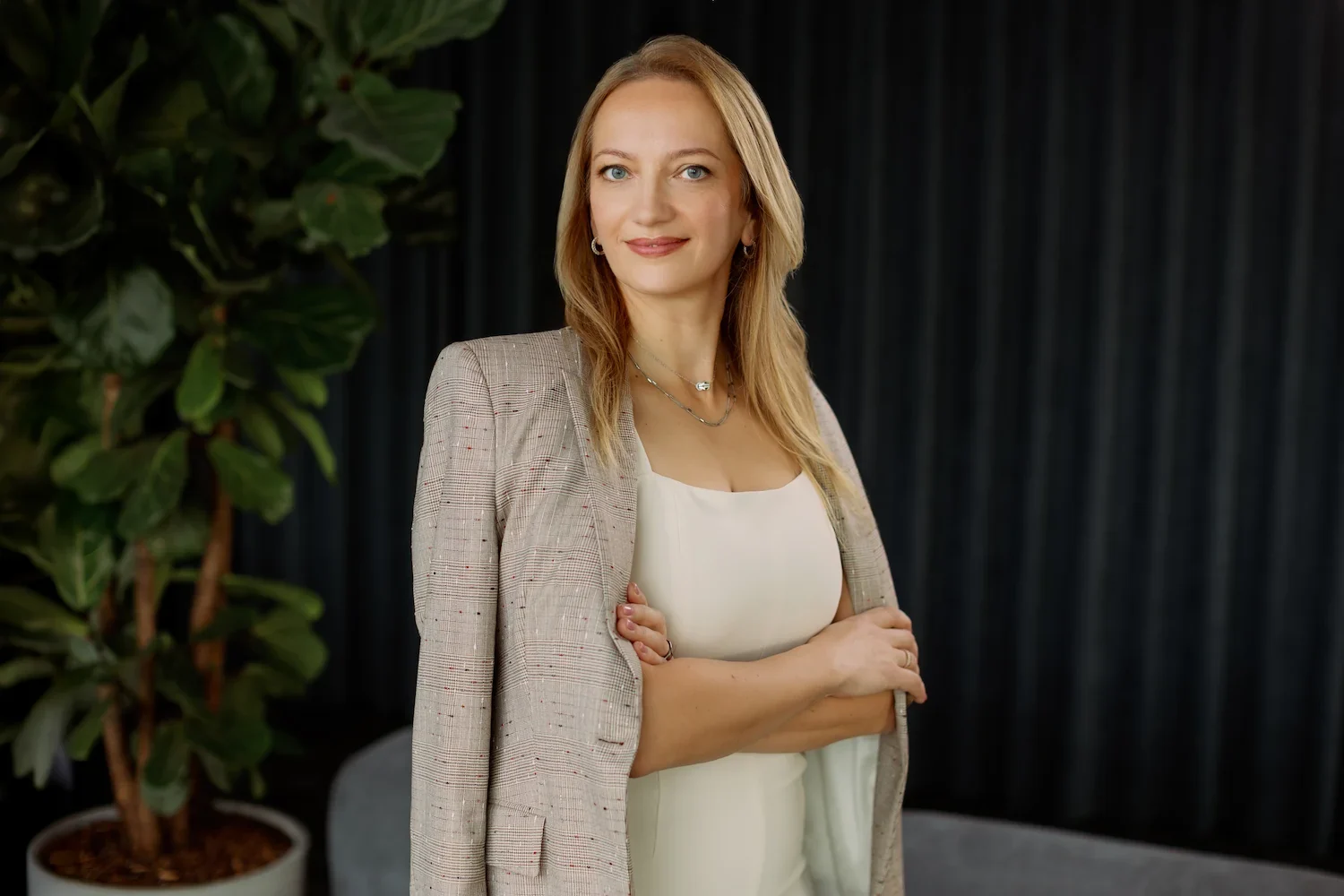 Business-Porträt einer Frau im schwarzen Blazer mit verschränkten Armen vor dunklem Hintergrund