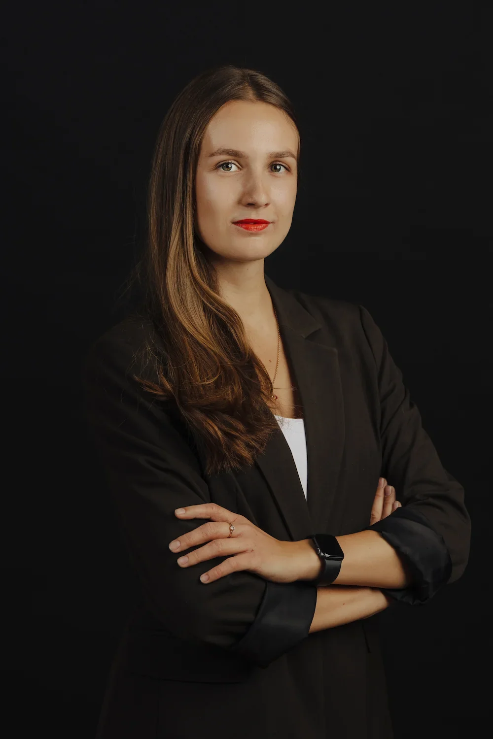 Business-Porträt einer Frau im schwarzen Blazer mit verschränkten Armen vor dunklem Hintergrund